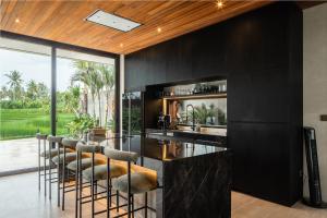 une cuisine avec des armoires noires et un bar avec des tabourets dans l'établissement Villa Famara Pererenan by Blacksand, à Tumbak Bayuh