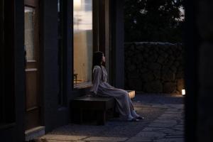 a woman sitting on a bench looking into a window at Generous Jeju in Jeju