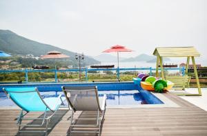 a swimming pool with chairs and umbrellas next to a pool at Geoje Harakeke Pension in Geoje