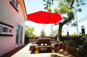 a picnic table with a red umbrella on a patio at Jeju Casalinda in Myŏngwŏl