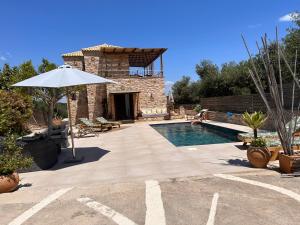 a swimming pool with an umbrella next to a house at Peroulia Stone Villa Koroni - Grèce, Péloponnèse in Koroni
