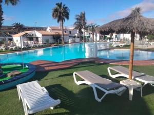 a swimming pool with two chairs and an umbrella at Puerta del sol in Caleta De Fuste