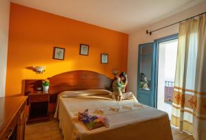 a little girl sitting on a bed in a hotel room at Hotel Bia Maore in Baunei
