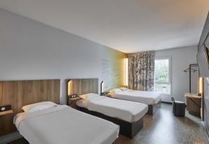 a hotel room with three beds and a window at B&B HOTEL Ouistreham in Ouistreham