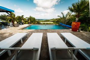 una piscina con due panche bianche in un resort di Bas de villa le rêve éveillé a Le Robert