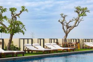 a pool with chaise lounges and chairs next to trees at Swiss-Belhotel Airport Yogyakarta in Yogyakarta