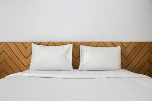 a bed with two white pillows and a wooden headboard at Minimalist and Cozy 1BR Patraland Urbano Apartment By Travelio in Bekasi