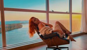 a woman sitting on a chair in front of a window at Ezza Experience - Beach Flat in Recife