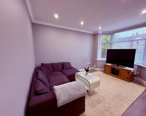 a living room with a purple couch and a flat screen tv at Cozy 3 bed house in Coventry