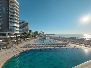 a swimming pool next to a beach with chairs and the ocean at GRIFID Noa in Golden Sands