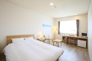 a bedroom with a large white bed and a desk at Ishigakijima Hotel Cucule in Ishigaki Island
