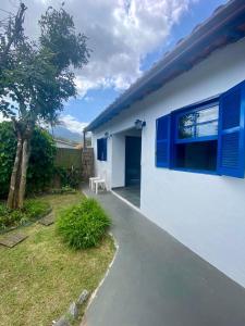 una casa bianca con finestre blu e un albero di Edícula Simples, prático e ideal a Ilhabela