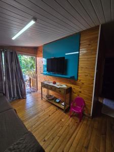 Una sala de estar con una mesa y un televisor en una pared. en Casa Rústica Iguaçu, en Foz do Iguaçu