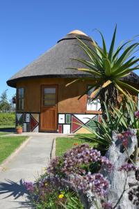 een huis met een rieten dak en bloemen ervoor bij African Sun Guest House in Molen Drift