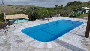 a blue swimming pool on a patio with two chairs at Chalés Vila Real - Tranquilidade na Serra de Carrancas - Piscina com uma vista espetacular do Pôr do Sol in Carrancas