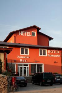 Hotel Romantik في Bălăuşeri: فندق برتقالي فيه سيارات تقف امامه