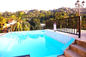 a blue swimming pool with a fence and trees at Ceylon Ayu Resort Kandy in Kandy