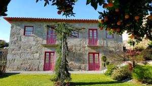 una antigua casa de piedra con puertas rojas y un naranjo en Quinta de Padreiro, en Arcos de Valdevez
