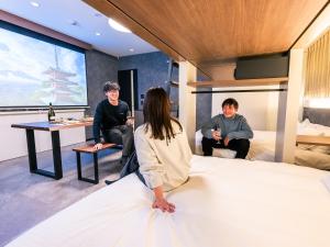 eine Gruppe von Personen, die in einem Zimmer um ein Bett herum sitzen in der Unterkunft HOTEL ALL IN TOKYO Asakusabashi in Tokio + 24 Fotos