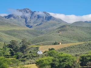 a small white house on a hill with mountains at Landsrivier Farmstyle Cottage No 2 in Uniondale +13 photos