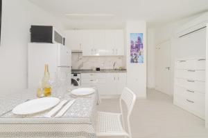a white kitchen with a table and white chairs at Buhardilla con terraza acogedora in Coslada