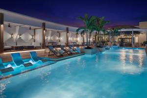 a swimming pool at night with blue chairs and palm trees at The Ben, Autograph Collection in West Palm Beach
