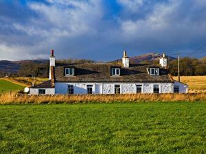 une maison blanche avec un toit noir dans un champ dans l'établissement Arthur's Cottage, à Dumfries