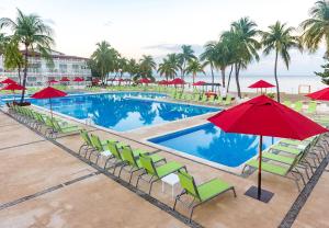 a swimming pool with green chairs and red umbrellas at Royal Decameron Indigo - All Inclusive in Montrouis