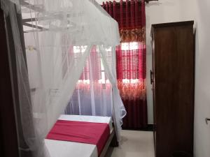 a bedroom with a bed with a canopy and red curtains at Thisumi Guest in Weligama