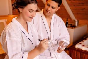 a man and a woman in white robes looking at a glass at Chalé Cruzeiro do Sul, hidromassagem, 2 min Thermas Machadinho-RS#3 in Machadinho