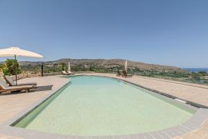 a large swimming pool with chairs and an umbrella at Villa Lefkothea in Georgioupoli