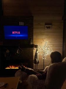 a woman sitting in front of a fireplace with a tv at Villa Prive and Spa in Kopaonik