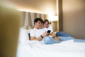 two people sitting on a bed looking at a cell phone at Courtyard by Marriott Munich City Center in Munich