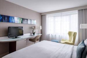 a hotel room with a bed and a desk with a television at Courtyard by Marriott Munich City Center in Munich