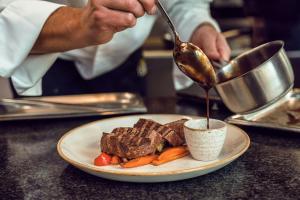 a chef is pouring sauce onto a plate of meat and vegetables at Courtyard by Marriott Munich City Center in Munich