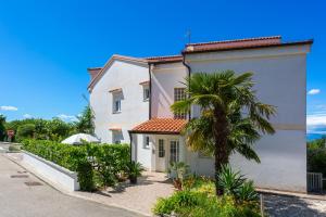 a white house with a palm tree in front of it at Apartments by the sea Njivice, Krk - 5295 in Njivice
