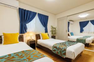 a hotel room with two beds and blue curtains at 恩納村一棟貸し ビーチや飲食店徒歩圏内 最大6名 Ciel希望ヶ丘A棟 in Onna