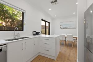 a white kitchen with white cabinets and a window at Stylish 3-Bed House Close to Attractions in Glenelg