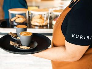 a person holding a plate with two cups of coffee at Pullman Auckland Airport in Auckland
