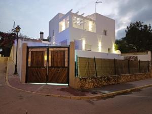 a white house with wooden gates and a fence at Villa Alhamar con piscina climatizada privada in Punta Umbría