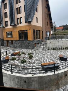 Šumska staza Divčibare apartmani في ديفشيبار: مبنى به مقاعد وأشجار في ساحة الفناء