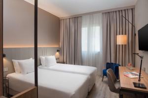 a hotel room with two beds and a desk at NH Trieste in Trieste