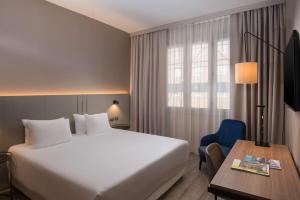 a hotel room with a bed and a desk and a window at NH Trieste in Trieste