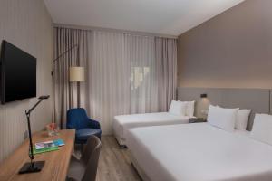 a hotel room with two beds and a desk and a tv at NH Trieste in Trieste
