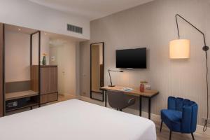 a hotel room with a bed and a desk and a tv at NH Trieste in Trieste