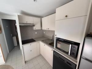 a small kitchen with white cabinets and a black microwave at Charmante Villa de vacances in Cap d'Agde