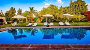 a swimming pool with white chairs and umbrellas at Villa Baddi Marrakech in Marrakesh