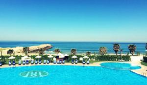 einen Pool mit Sonnenschirmen und Stühlen sowie das Meer in der Unterkunft Grand Mogador Sea View & Spa in Tangier