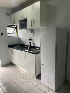 cocina con armarios blancos, fregadero y nevera en Grace Villas 28, en East London