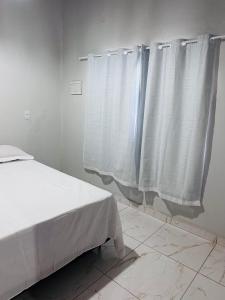 Vila Limeira في بورتو سيغورو: غرفة نوم بسرير ونافذة ذات ستائر بيضاء